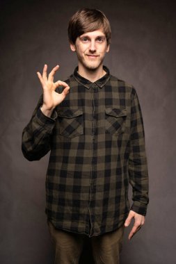 Genç yakışıklı, uzun boylu, zayıf, kahverengi saçlı, gri arka planda flanel gömlekli, tamam yazan beyaz adam.