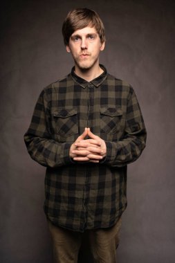 Genç yakışıklı, uzun, zayıf, beyaz, kahverengi saçlı, flanel gömlekli, gri arka planda dikkatsiz bir adam.