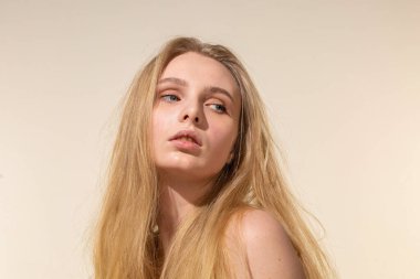 Sarı saçlı, bej renkli portrede çıplak makyajlı genç bir kadın.