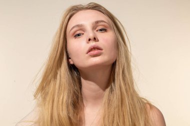 Beyaz, genç, sarı saçlı, bej renkli, çıplak makyajlı bir kadın.