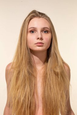 Uzun sarı saçlı beyaz kadın bej portrede izole edilmiş.