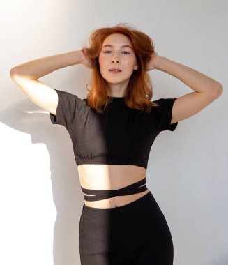 Kızıl saçlı genç bir kadın. Gri üzerinde yalnız. Elleri başının arkasında duruyor.