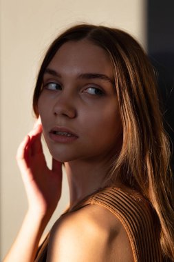 Gün batımında çekilmiş bir portre. Koyu saçlı, beyaz tenli, bej renkli, yüzü gölgeli bir kadın.