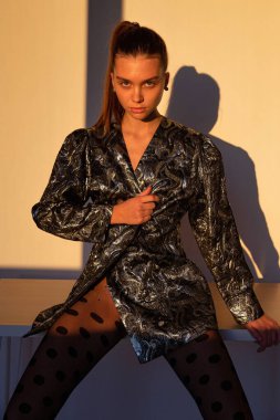 Gün batımında, siyah saçlı, beyaz tenli, arkasında keskin gölgeler olan bir kadın.