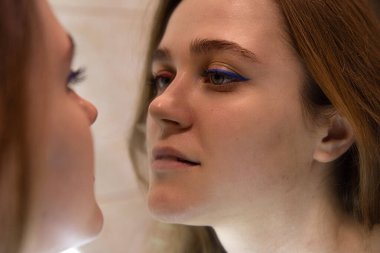 Aynadaki beyaz tenli genç kadın mavi göz kalemi kullanmış.