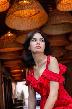 Siyah saçlı, beyaz tenli, kırmızı noktalı elbiseli genç bir kadının portresi.