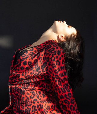 Siyah saçlı, beyaz tenli, esmer, leopar desenli elbiseli bir kadın.