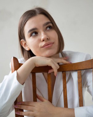 Beyaz Avrupalı kadın portresi, kısa saçlı beyaz takım elbiseli bir sandalyede oturuyor.