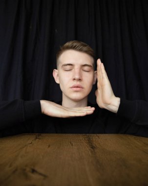 Siyah üzerine izole edilmiş genç sarışın adam portresi masanın üzerinde yüzünün yakınında el ele tutuşuyor.