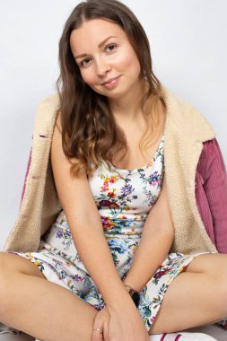 Bahar pembesi renkli genç bir kadın. Beyazlar içinde izole edilmiş. Ayakları çapraz yerde oturuyor.