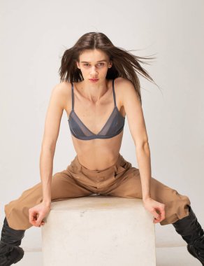 Koyu renk düz saçlı, genç, zayıf bir kadın. Bej renkli, bacakları ayrık.