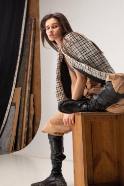 Stüdyoda omuzlarında ekose ceketiyle oturan zayıf bir kadın.