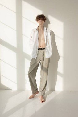 Duvarında pencere gölgesi olan yalınayak çekici Avrupalı genç adam