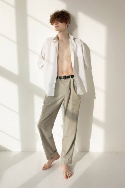 Duvarında pencere gölgesi olan yalınayak çekici Avrupalı genç adam