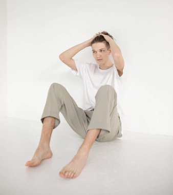 Çıplak ayaklı, çekici Avrupalı bir adam bej renginde izole bir şekilde yerde oturuyor.