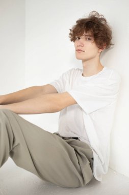 Çekici genç Avrupalı adam bejde izole edilmiş beyaz gömlekli yerde oturuyor.