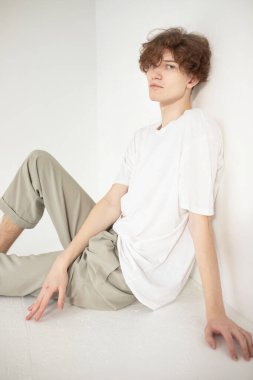 Çekici genç Avrupalı adam bejde izole edilmiş beyaz gömlekli yerde oturuyor.