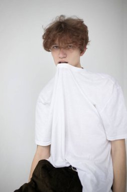 Çekici genç Avrupalı adam açık gri üzerinde izole edilmiş gömleğini dişleriyle çıkarıyor.