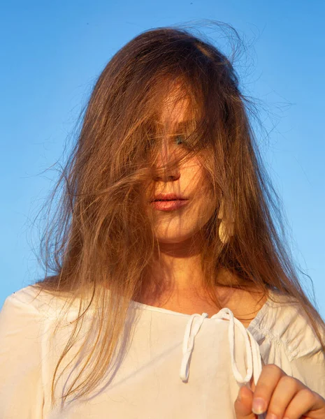 Beyaz tenli, arkasında gökyüzü olan, yüzünde kılları olan genç bir kadın.