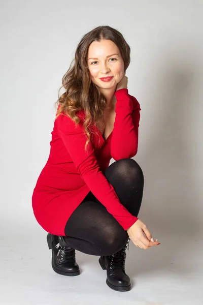 魅力的な若いヨーロッパの女性を下にスクワット赤いドレスでグレーに隔離 — ストック写真