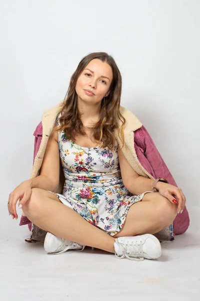穿着春色衣服的年轻女人穿着淡灰色的衣服 双腿交叉地坐在地板上 — 图库照片