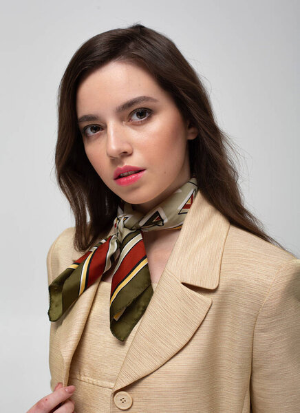 Portrait of european woman with dark hair in beige suit with bright silk scarf isolated on light grey