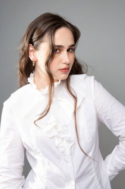 Uzun saçlı, koyu kahverengi gözlü, beyaz bluzlu, gri elbiseli genç bir kadın.