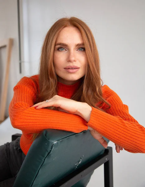 Stock image Woman with long red hair in orange jumper leaning on chair with folded arms