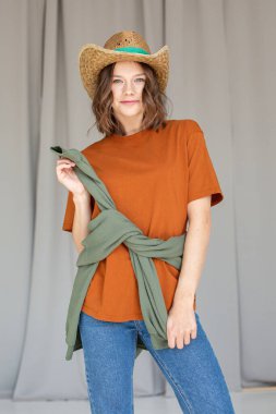 Sırıtkan beyaz Avrupalı genç bir kız, şapkası stüdyoda, belinde bir kazakla dikiliyor.