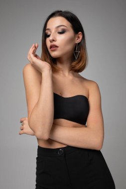 Kısa siyah saçlı zayıf genç kadın koyu gri üzerinde tek başına duruyor.