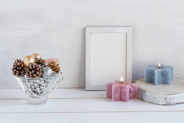 Christmas decoration, mock up in a white frame with a composition of cones and new year beads, candles on a white table, copy space. High quality photo