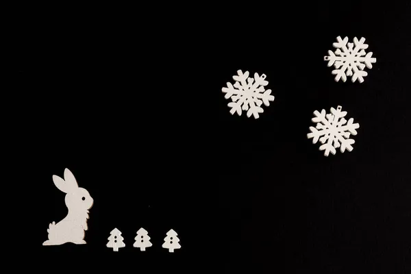 Compoziție elegantă de Crăciun pe un fundal negru, figurine din lemn de iepure, fulgi de zăpadă și pomul de Crăciun, spațiu de copiere — Fotografie, imagine de stoc