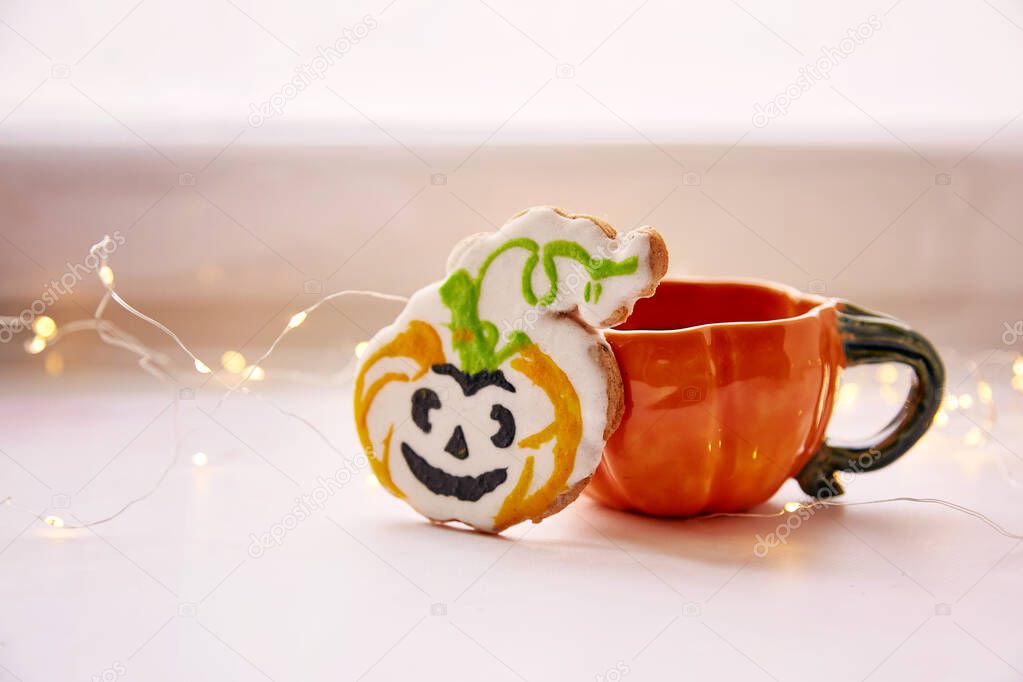 Halloween cookies. Pumpkin cup and homemade cookies in shape of cute pumpkins. Atmospheric aesthetic autumn mood or trick or treat concept. Copy space. Home cooking and coziness