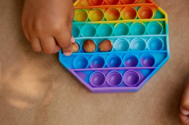 Toddler pop it toy ve ela ile oynuyor. Motor becerilerin geliştirilmesi oyunu. Gökkuşağı dokunuşu duyusal dokunuş. Üst Manzara. Yüksek kalite fotoğraf