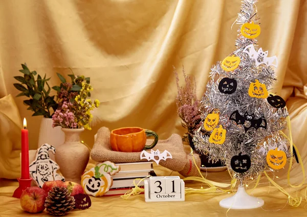 Autumn holidays. Aesthetic home party with trendy Halloween tree and decorations. Cozy Halloween with candles, orange mug, dry flowers, cookies in shape of pumpkin and ghost with books and calendar