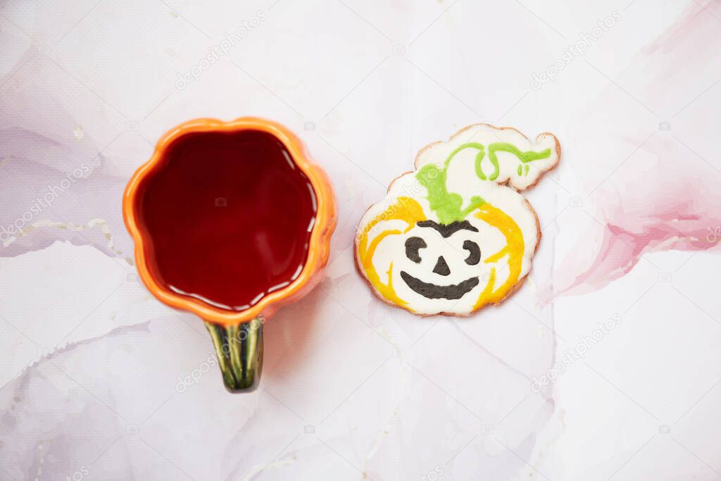 Halloween creative concept: pumpkin cup and homemade cookie in shape of cute pumpkin closeup. Aesthetic autumn mood or trick or treat concept. Autumn cozy home concept