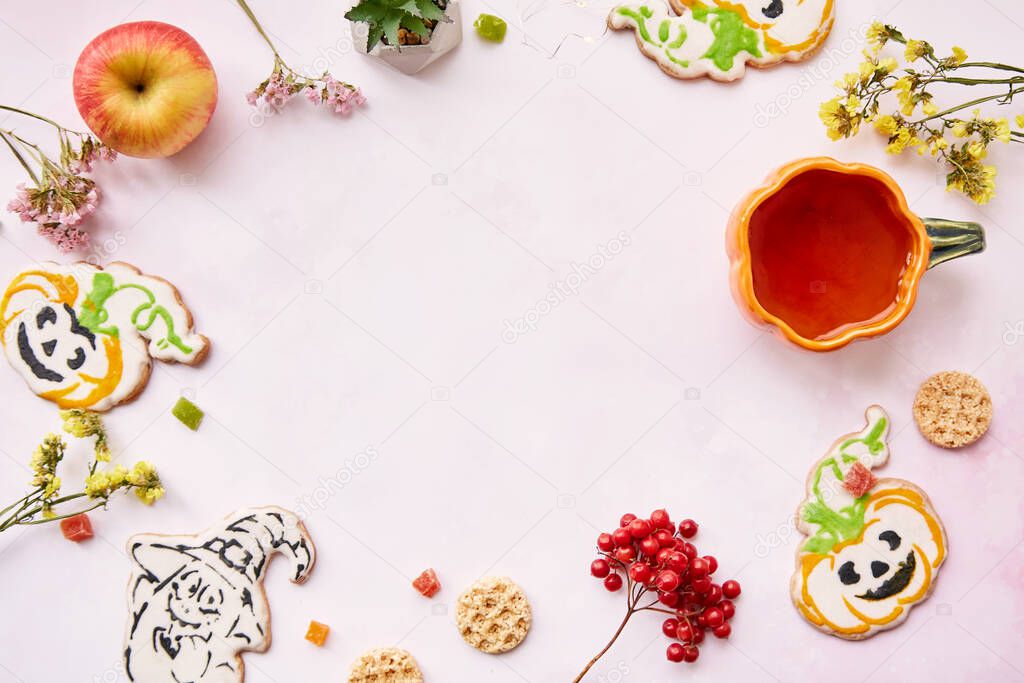 Halloween festive background: pumpkin cup and cookies in shape of cute pumpkins and ghost. Atmospheric aesthetic autumn mood or trick or treat concept. Apples, dry flowers and candied fruit.