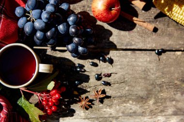 Sonbahar arkaplanı: üzümler, elmalar, viburum, frenk üzümü, çay fincanı ve ahşap masanın üzerinde yüksek açılı gölgeli tarçın çubukları. Şükran Günü konsepti. Açık hava sonbahar estetiği. Boşluğu kopyala.
