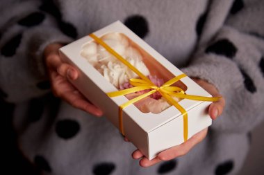 Kadın elleri, içinde pembe ve beyaz şekerlemeler olan bir hediye kutusu veriyor. Boks günü konsepti. Sıcak kış hafta sonları. Ev yapımı tatlılar..