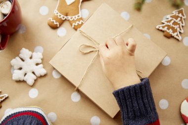 Çocuk hediye kutusunu tutuyor. El işi dekorasyonu, zencefilli kurabiye, köknar ağacı dalı, marşmelovlu sıcak içecek ve Noel süsleri. Moda tarzı. Mutlu Noeller. Yüksek kalite fotoğraf