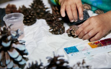 Bir çocuğun yılbaşı konilerini boyaması. Çocuklara öğretmek, motor becerilerini geliştirmek. Küresel el işi hobisi. Noel için hazırlanıyorum. Doğal süsler. Yüksek kalite fotoğraf