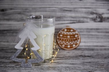 Güzel bir Noel geleneği. El yapımı taze kurabiyeler ve ahşap masada sıcak bir bardak süt. Masa ayarı. Noel şenliği havası ve çelenkli estetik atmosfer. Boşluğu kopyala.