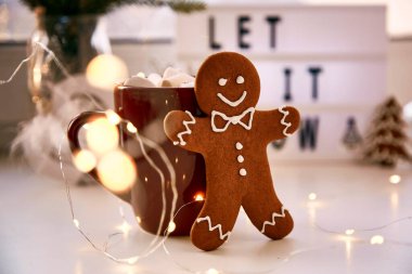 Ev yapımı zencefilli kurabiye, üzerinde şenlikli bokeh dekoru var. Kar arka planda kalsın. Sıcak içecek ve marşmelovlu Noel süsleri. Estetik Noel atmosferi, ev konforu, sıcaklık konsepti