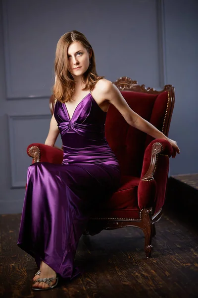 Çekici, beyaz bir kadın, klasik koltukta. Evin içi rahat. Klasik iç estetik.