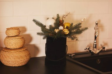 Mutfak lavabosu ve hasır sepetlerin yanındaki masada Noel süsleri. Akşam ışığında ev mutfağı..