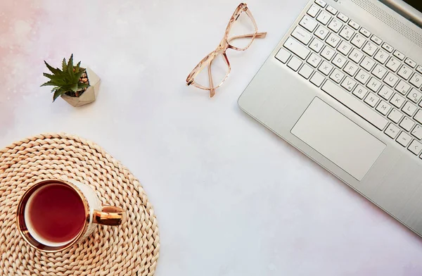 Aesthetic home office: laptop, tea cup and glasses. Feminine concept, remote work, freelance, taking webinar, video calling family because of quarantine concept. Copy space, view from above.