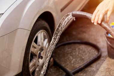 Arabayı hortumların altından suyla yıkamak. Ev rutinleri. Araç bakımı.