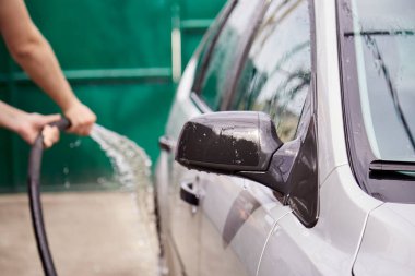 Bahar temizliği konsepti. Arabayı hortumların altından suyla yıkamak. Ev rutinleri. Araç bakımı.