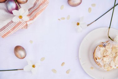 Paskalya arkaplanı çok zarif. Mor renkli ve turuncu renkli yumurtalar, narsis çiçekleri ve badem taneleri. Paskalya pastası. Üst görünüm, alanı kopyala.