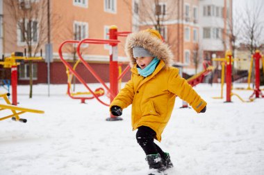 Mutlu gülümseyen çocuk şehirde karda eğleniyor. Kış eğlencesi dışarıda. Parlak turuncu kışlık ceketli çocuk. Mutlu bir çocukluk. Kış mevsimi. Yüksek kalite fotoğraf